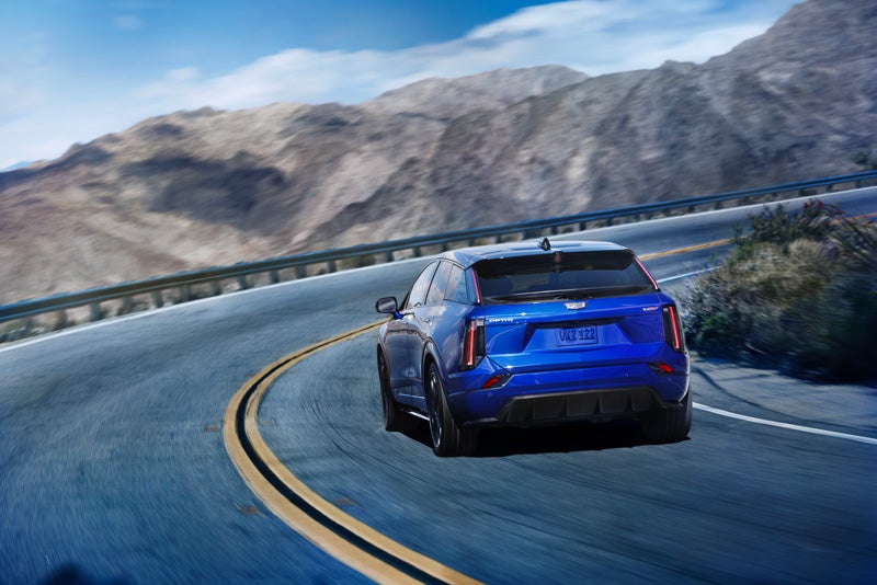 Rear View of a Blue 2026 OPTIQ-V Driving on a Curve of a Mountain Row | Corwin Motors Kalispell Cadillac in Kalispell MT